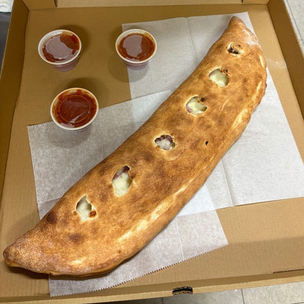 A long, golden-brown calzone with melted cheese peeking through, served with three cups of marinara sauce in a pizza box.