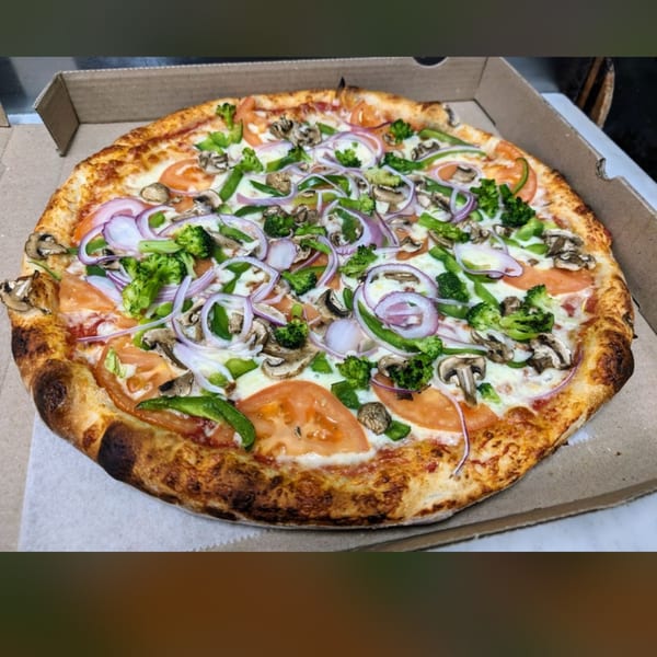 Shakey Jake's veggie pizza with broccoli, mushrooms, red onion, green peppers, and tomatoes in a box.