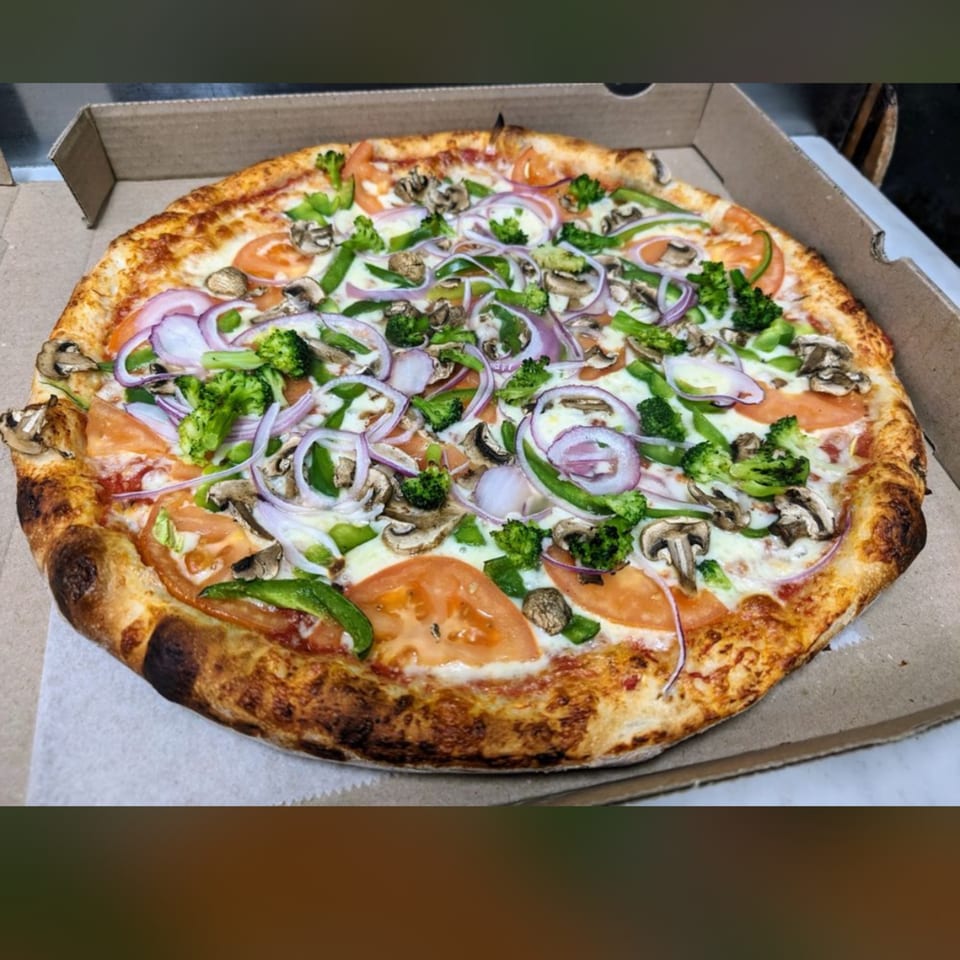 Shakey Jake's veggie pizza with broccoli, mushrooms, red onion, green peppers, and tomatoes in a box.