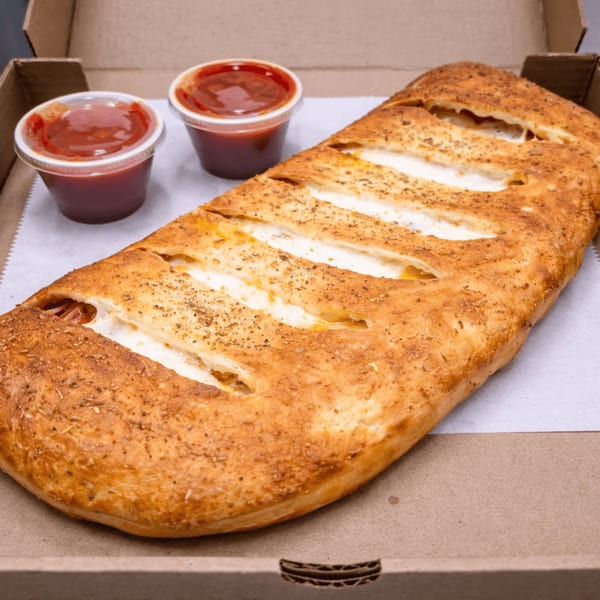 A golden-brown calzone with visible cheese and pepperoni, served with two cups of marinara sauce in a pizza box.
